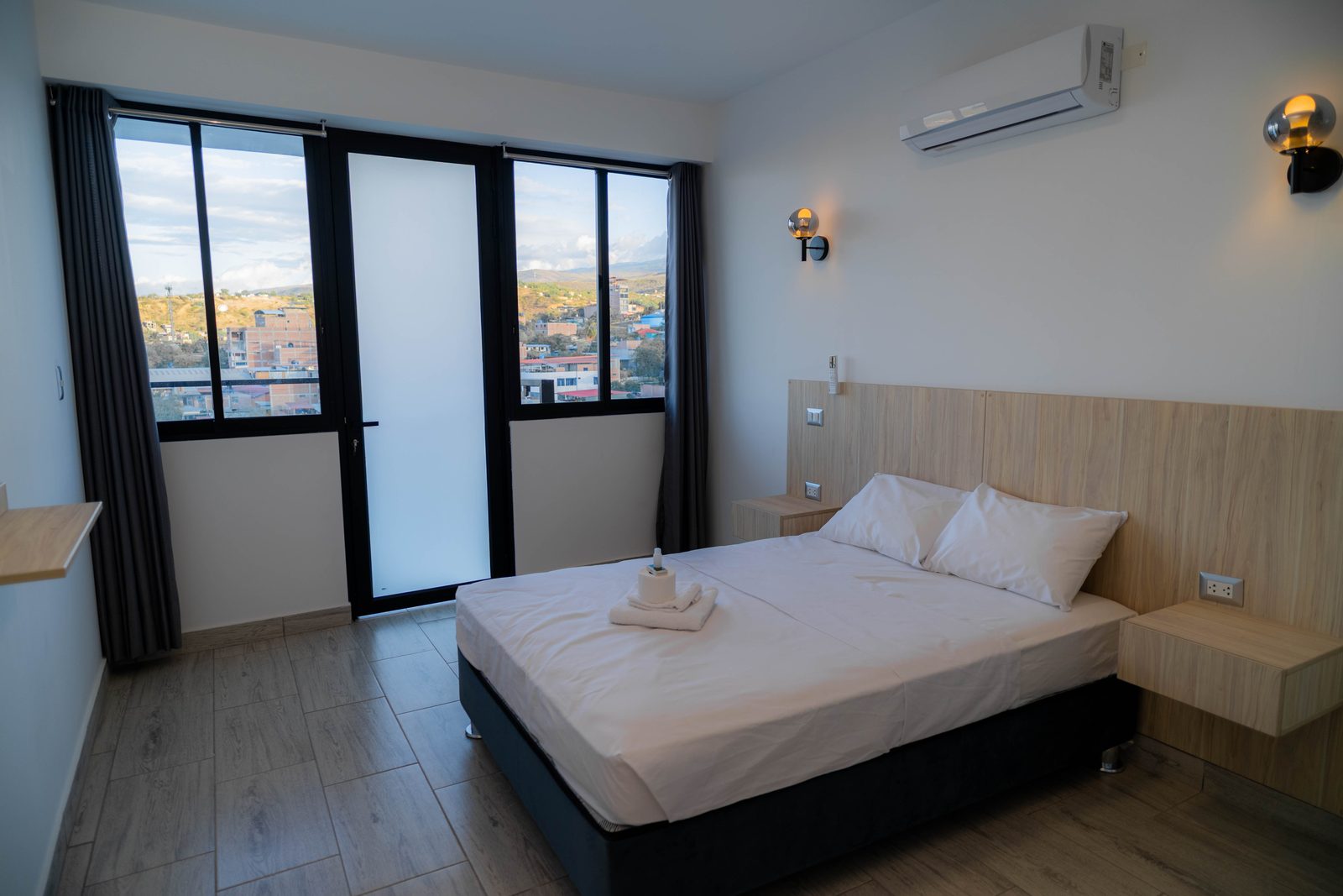 Dormitorio con cama matrimonial, balc&oacute;n y vista a la ciudad